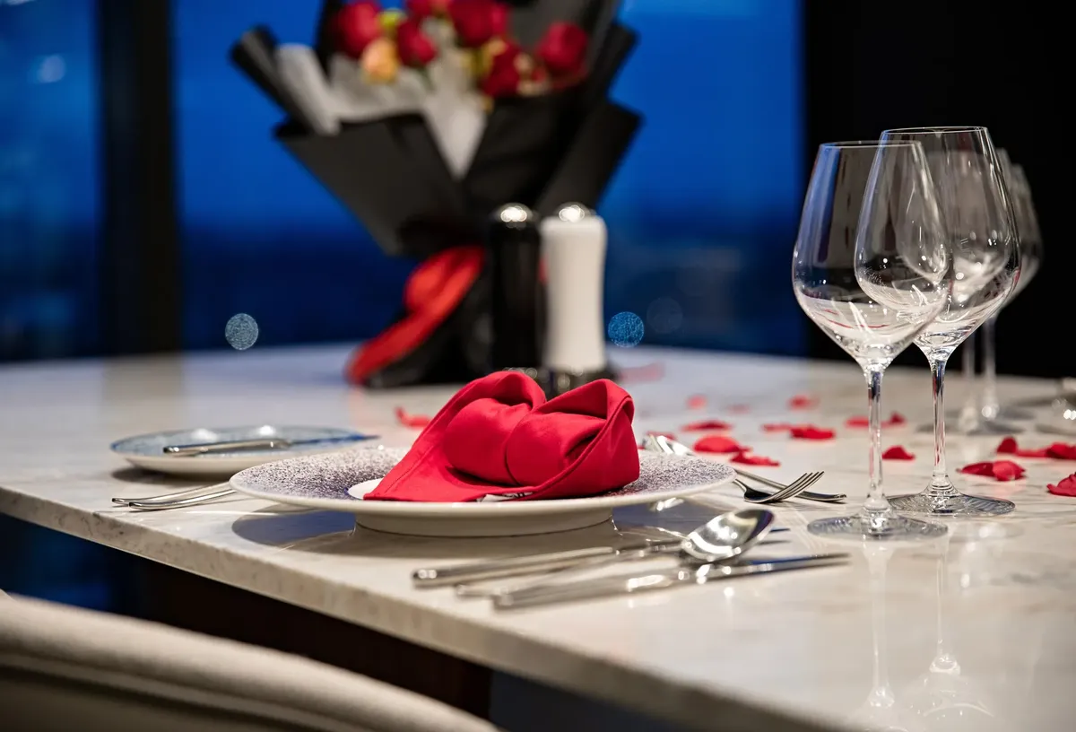Elegant romantic dinner setting with red roses petals and folded napkin, perfect for special occasions.