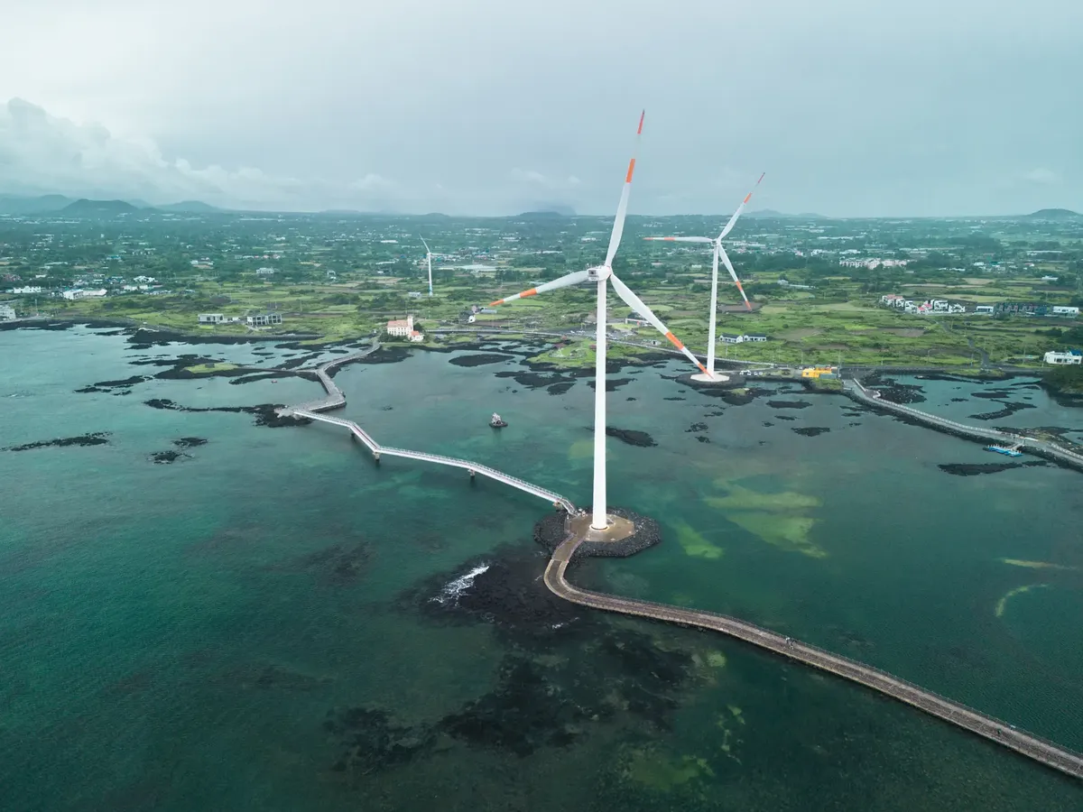 Scenic aerial shot of wind turbines along Jeju's coast, showcasing renewable energy.